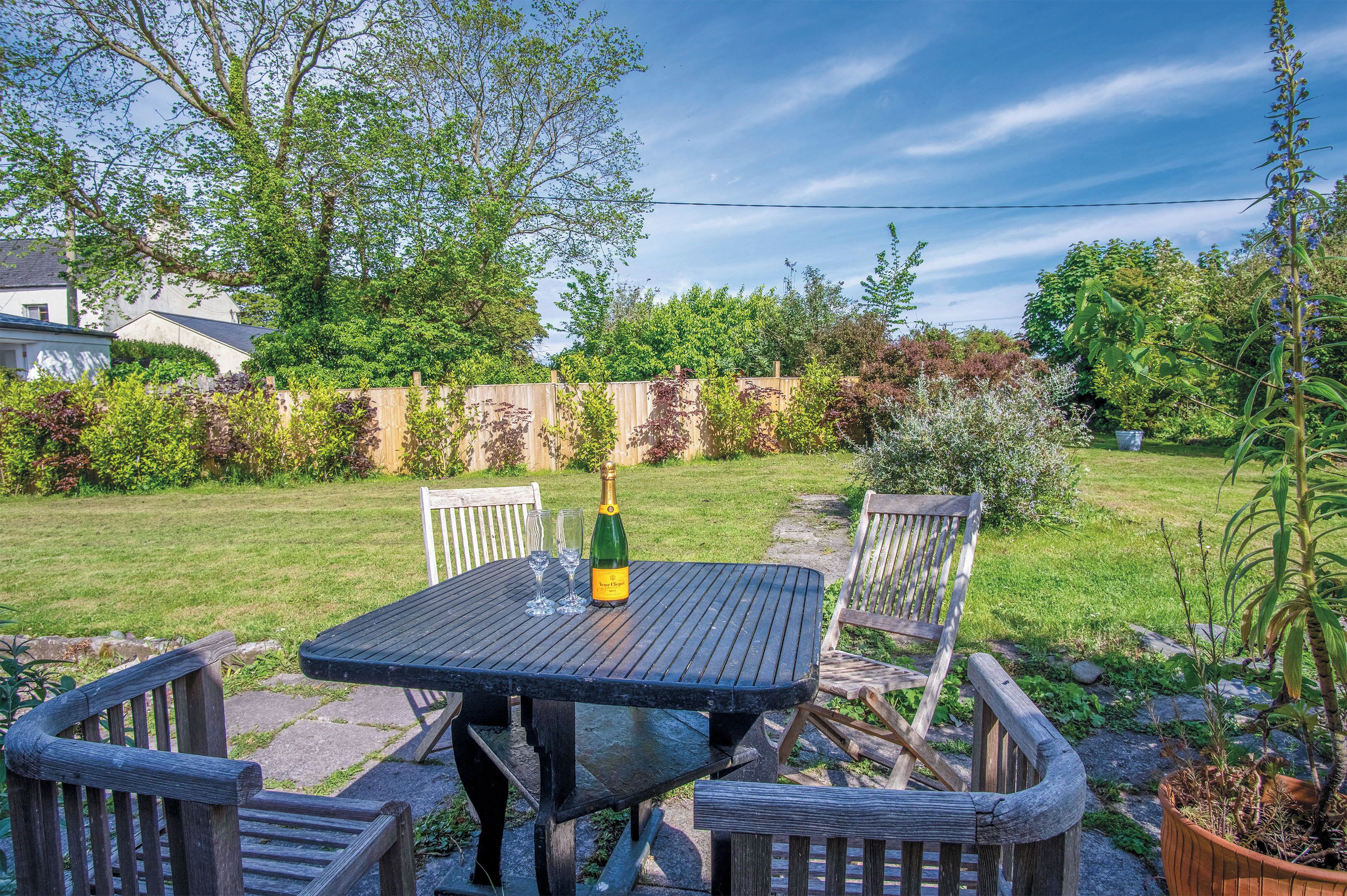 A wooden table with chairs in a backyard with a grassy lawn, a wooden fence, and various plants.