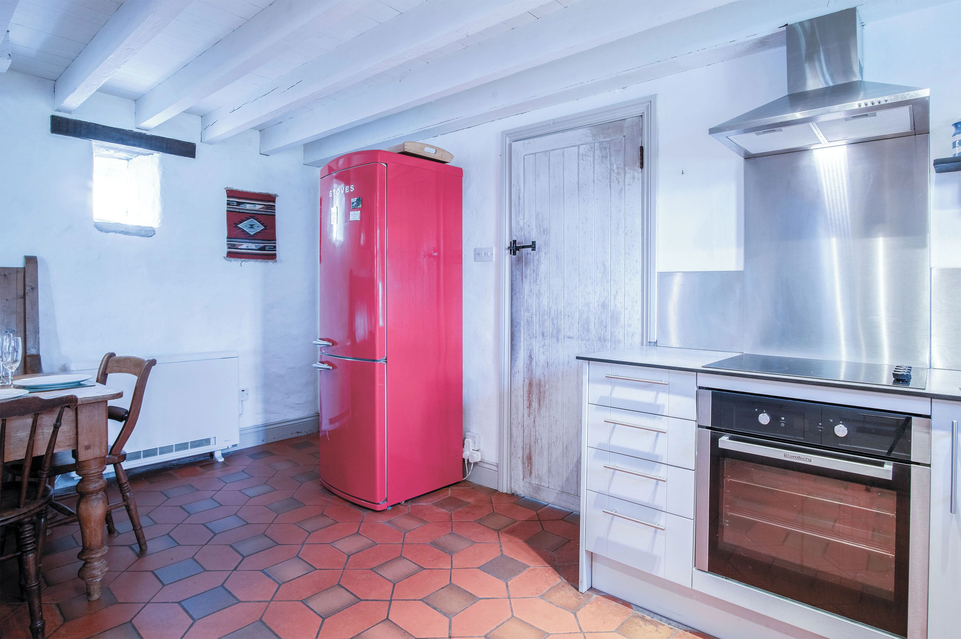A kitchen with a red refrigerator, a stainless steel oven, and a white cabinet.