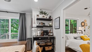 Un dormitorio moderno con una cama, una mesita de noche y una pequeña zona de kitchenette con estantes y una estación de café.