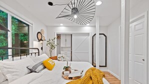Un dormitorio con cama, mesita de noche y ventana con vista a follaje.