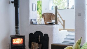 Um quarto aconchegante com lareira a lenha, uma cadeira de vime e uma escada que leva a um andar superior.
