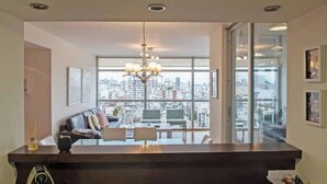 Un soggiorno moderno con un'ampia finestra vista sulla città, un tavolino da caffè in legno scuro e un lampadario.
