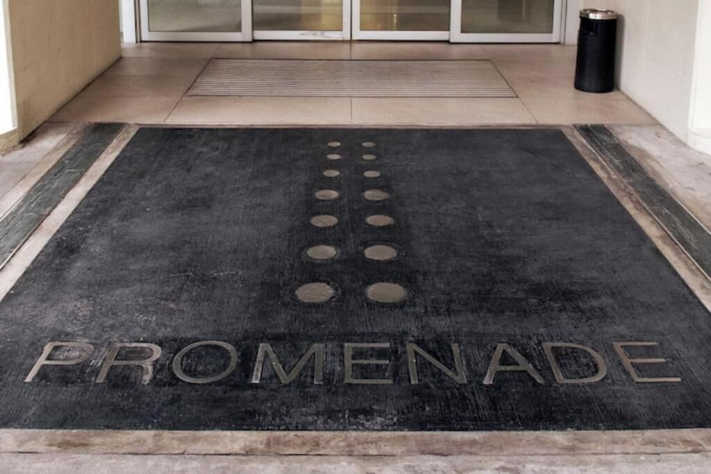 Eine schwarze Fußmatte mit der Aufschrift 'PROMENADE' in Metallbuchstaben.