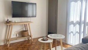 Una sala de estar con televisor de pantalla plana, una mesa de madera, una mesita redonda y un sofá.