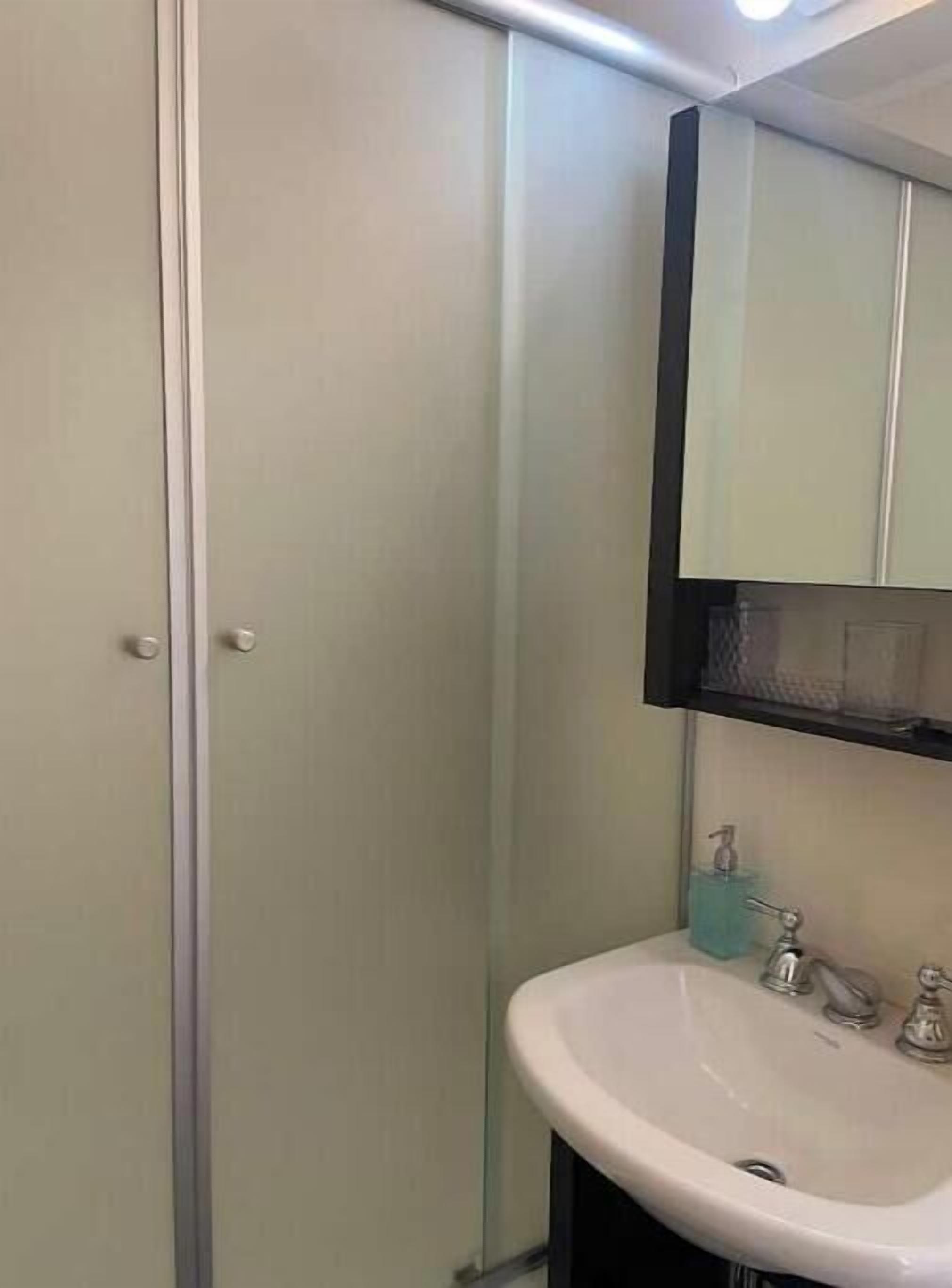 A bathroom with a glass shower enclosure, a sink with a mirror above it, and a soap dispenser on the sink.