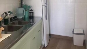 Una cocina con armarios verde claro, un refrigerador blanco, un lavabo y un bote de basura.