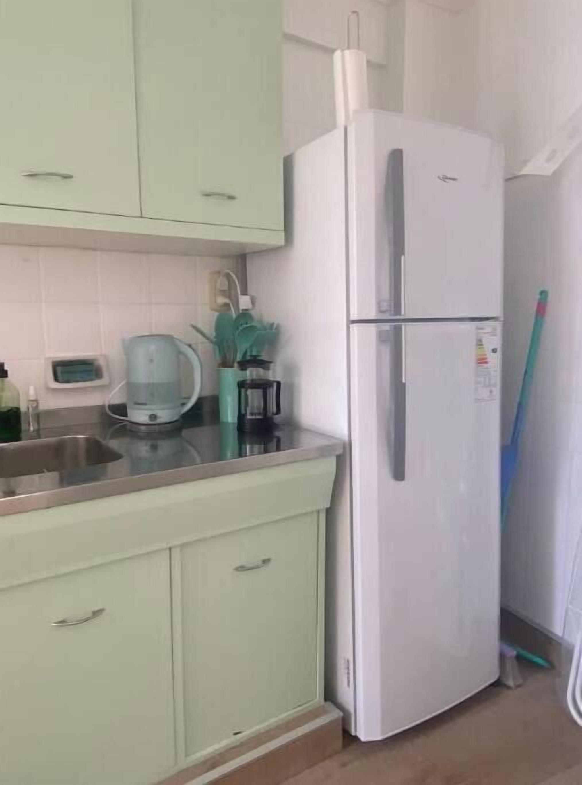 A kitchen with light green cabinets, a white refrigerator, a coffee maker, and a broom leaning against the wall.