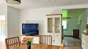 A dining area with a wooden table, chairs, a vase of flowers, a television, and a cabinet with glass doors.