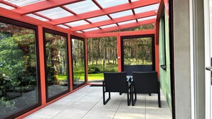 A covered patio with glass walls, a dining table, and chairs.