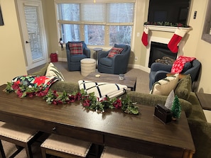 A cozy living room with a fireplace, two blue armchairs, a coffee table, and festive decorations. - Walk to everything, directly on the Chattahoochee River, in Alpine Helen, GA (Helen)