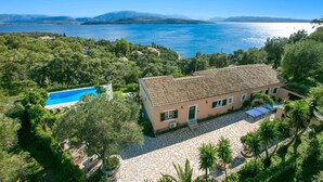 Una villa in stile mediterraneo con tetto in tegole, piscina e cortile pavimentato in pietra.