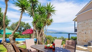 Patio esterno con tavolo e sedie, affacciato su un corpo d'acqua e montagne.