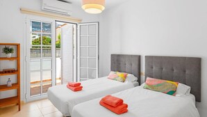 A hotel room with two beds, a wooden shelf with a plant, and a view of greenery through the open door. - Villa Costa Adeje by Villa Plus (Adeje)