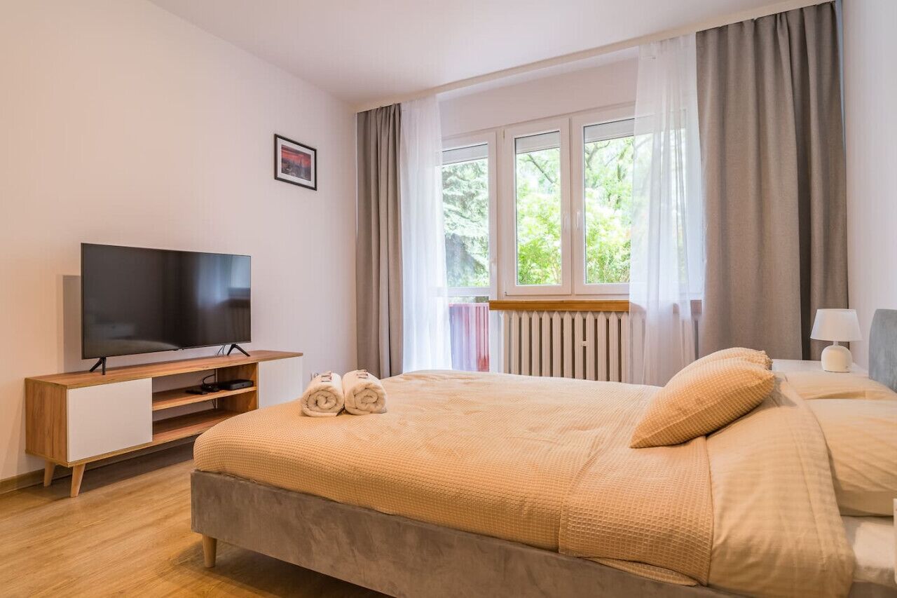 Habitación de hotel con cama, televisión, ventana con cortinas y radiador.
