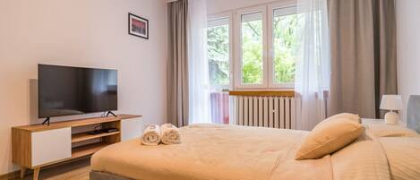 Habitación de hotel con cama, televisión, ventana con cortinas y radiador.