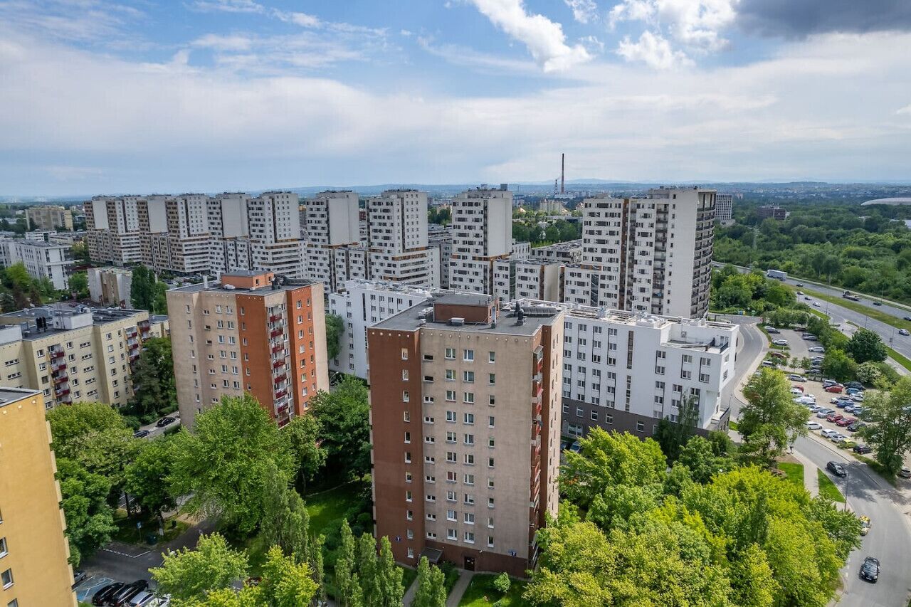Ein hoher Wohnkomplex mit mehreren Mehrfamilienhäusern, umgeben von Grünflächen und einer Straße mit parkenden Autos.
