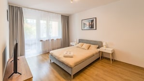 A modern bedroom with a large bed, a TV on a wooden table, and a window with curtains. - Kraków Czyżyny - Terrace & Workspace - by Rentujemy (Kraków)