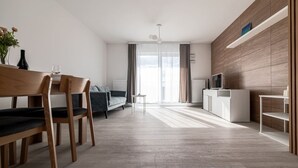 A modern living room with a dining area, a sofa, a TV, and a fireplace. - Witolda Riverside Apartments - Balcony, City View - by Rentujemy (Wroclaw)