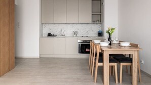 A modern kitchen with a marble backsplash, wooden cabinets, and a dining area with a table and chairs. - Witolda Riverside Apartments - Balcony, City View - by Rentujemy (Wroclaw)