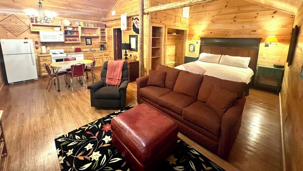Interior acollidor d'una cabana de fusta, amb zona de menjador, cuina i un llit gran.
