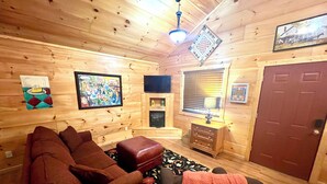 Interior acollidor d'una cabana amb un sofà marró, un petit reposapius, una televisió i una porta de fusta.