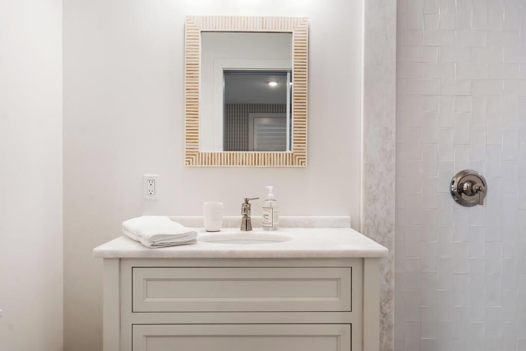 A bathroom with a white vanity, a mirror with a wooden frame, a towel, a soap dispenser, and a toilet paper holder.