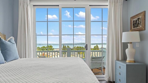 Un dormitorio con una cama grande, una mesita de noche, una lámpara y vistas al exterior a través de una ventana.