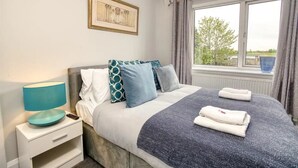 Quarto bem organizado com cama, mesa de cabeceira, luminária e janela com cortinas.