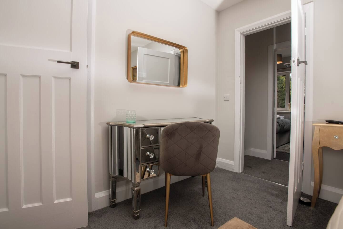 A room with a vanity, a mirror, and a door leading to another room.
