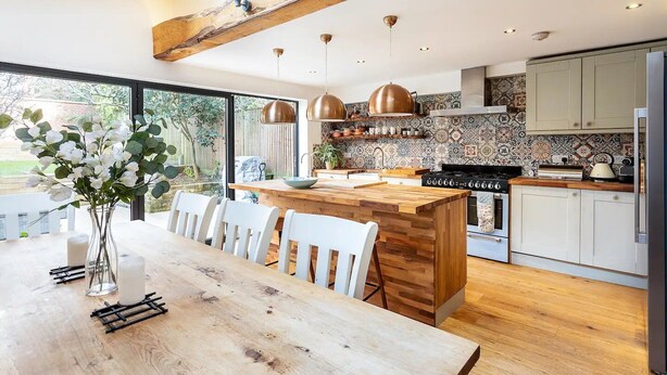 A modern kitchen with a wooden island, white chairs, and pendant lighting.