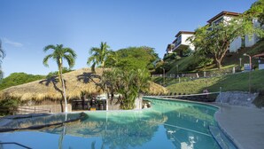 Una piscina en un entorno tropical, con palmeras y una estructura de techo de paja.