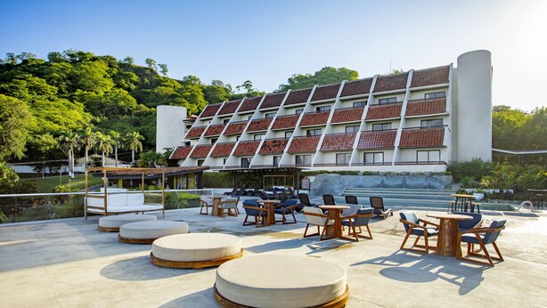 Una terraza en la azotea con asientos redondos, piscina y un edificio con tejados de tejas rojas.