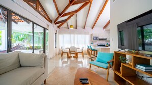 A spacious living area with a sofa, coffee table, and TV stand. There is a dining area with a table and chairs, and a kitchen in the background. - Villas Sol 21 Serenity Place at Playa Hermosa (Playa Hermosa)
