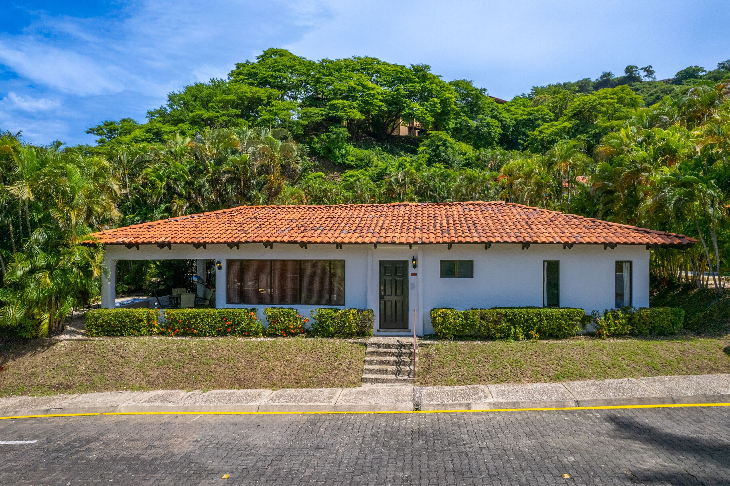 A single-story building with a tiled roof, surrounded by lush greenery and palm trees.