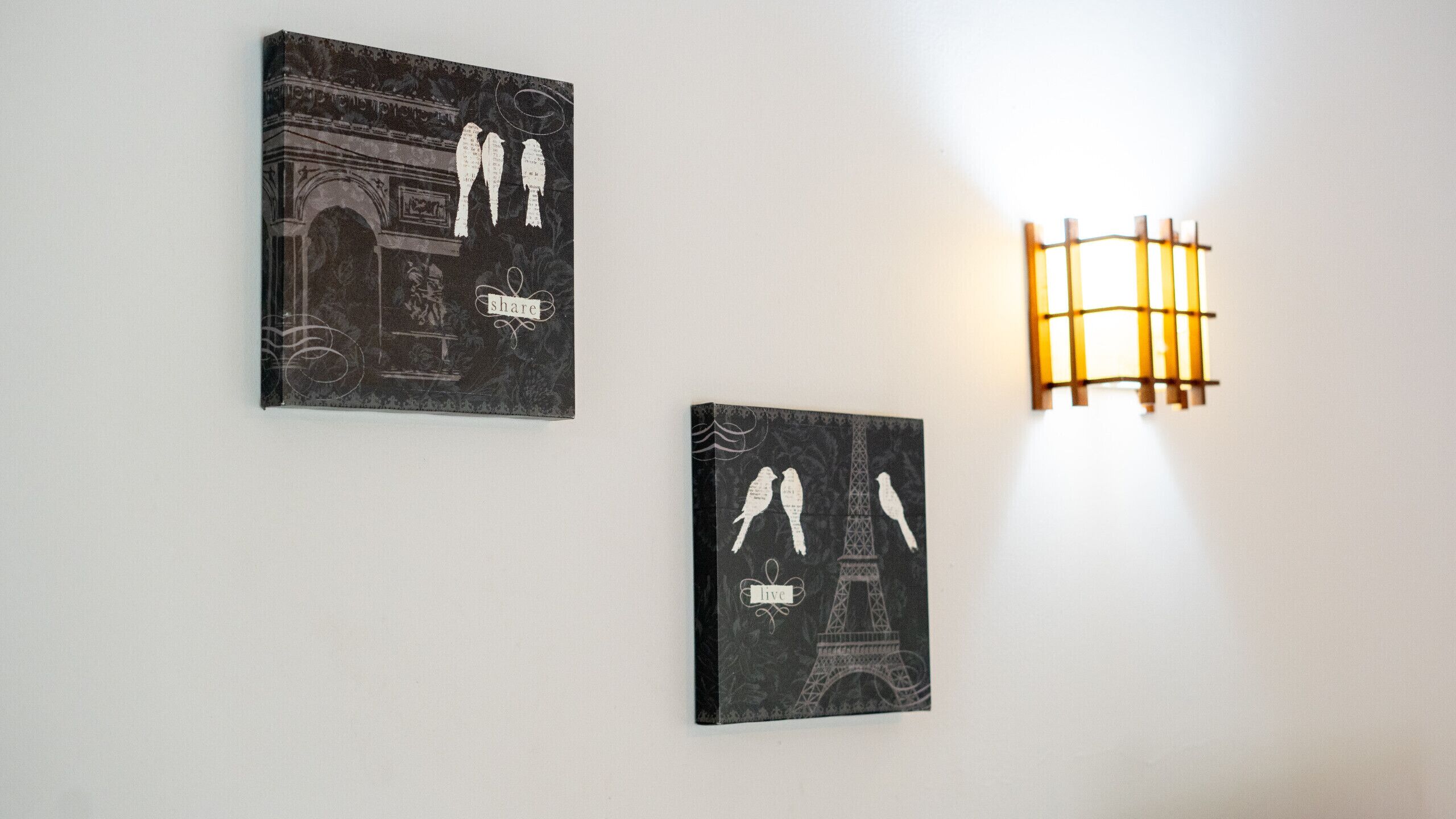 Two framed artworks depicting birds and the Eiffel Tower, mounted on a white wall.