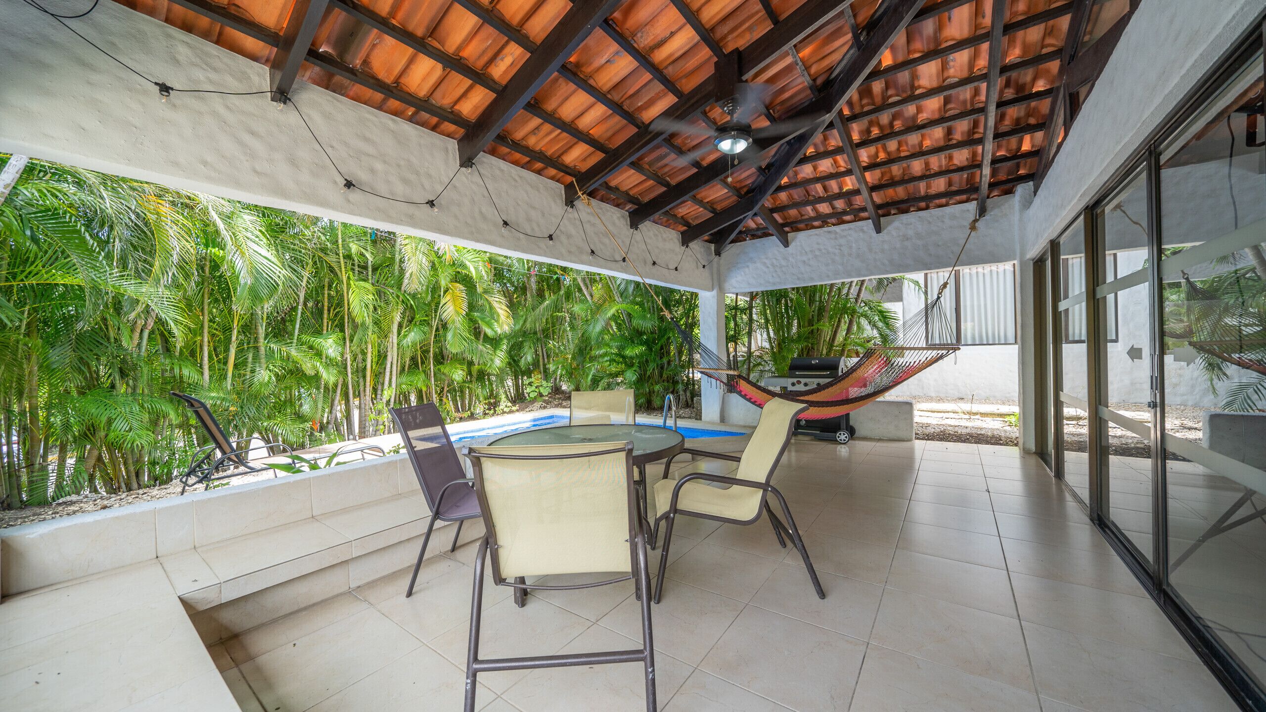 Une terrasse couverte avec une piscine, des chaises et un hamac.