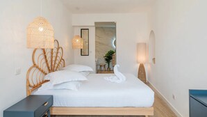 A modern bedroom with a wooden bed frame, white bedding, and a swan-shaped pillow. There are two wall-mounted lamps and a wicker pendant light.