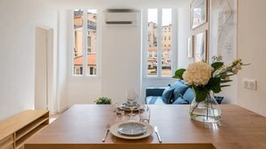A dining area with a wooden table set for two, a vase with flowers, and a city view through large windows.