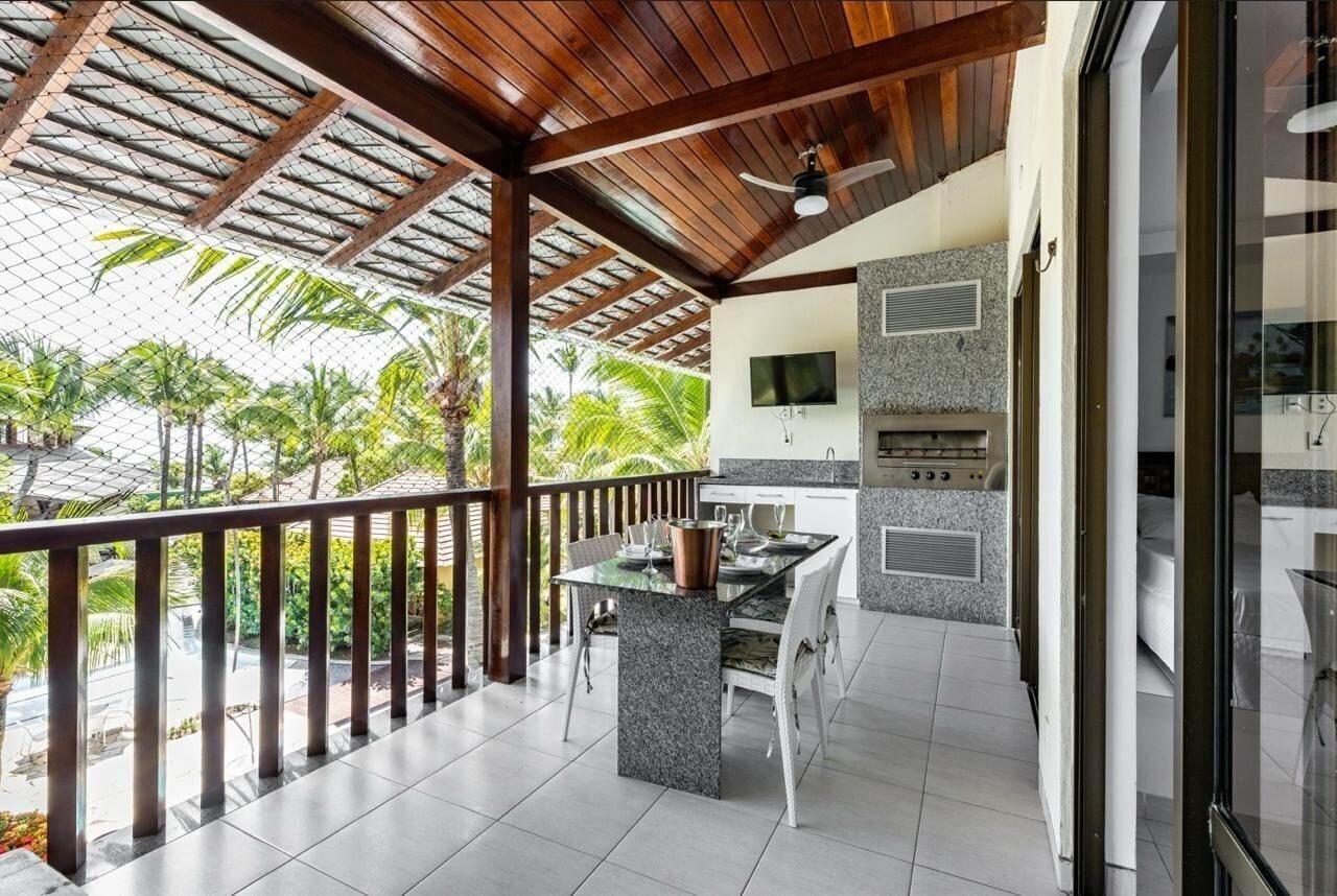 A covered outdoor area with a dining table and chairs, a grill, and a TV mounted on the wall.