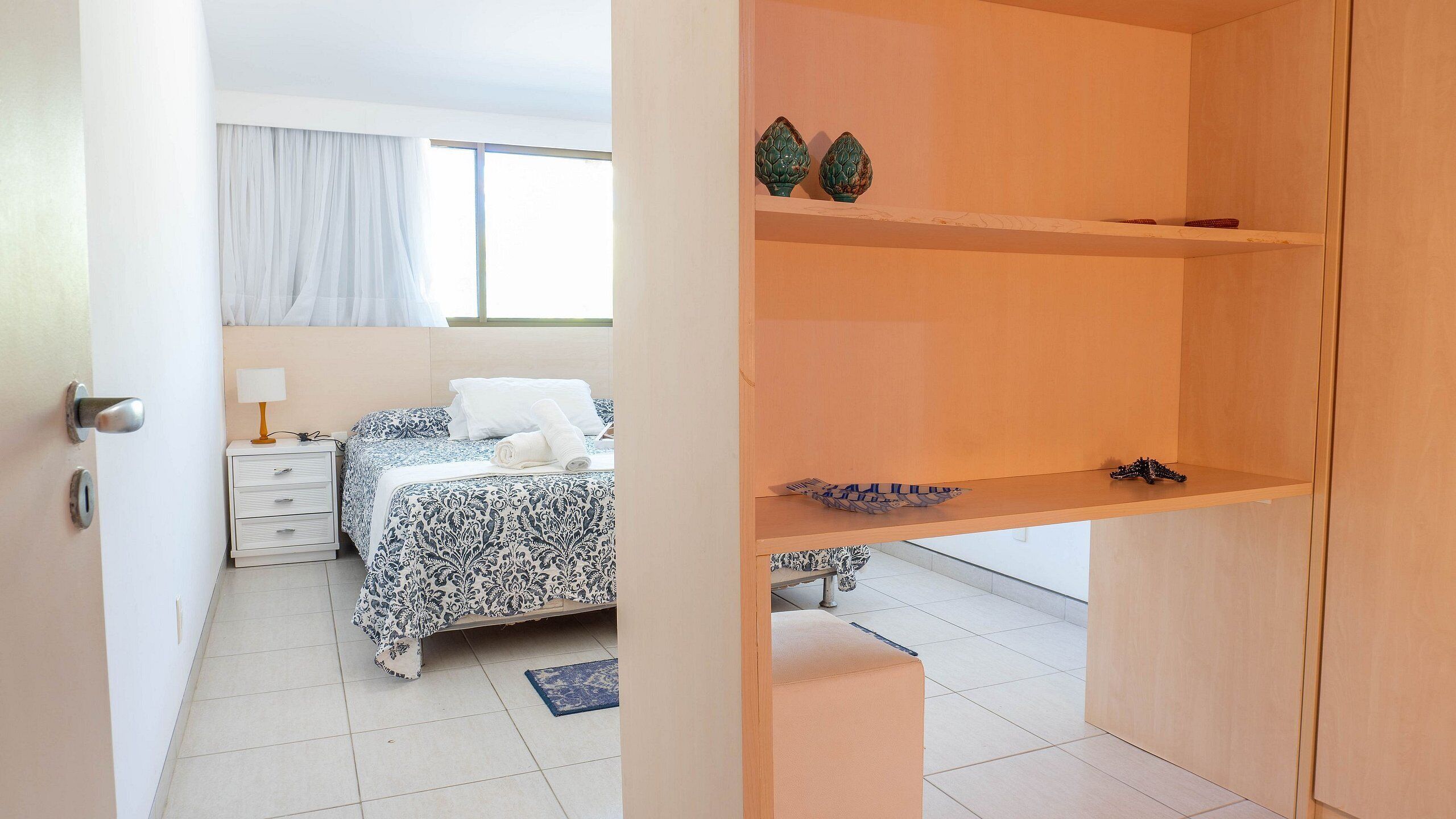 A bedroom with a bed, bedside table, lamp, and a window with curtains.