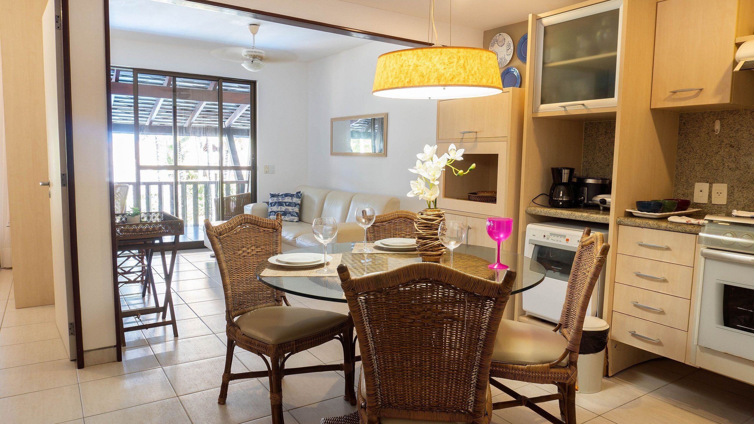 A dining area with wicker chairs and a glass table, a kitchen with white appliances, and a sliding glass door leading to an outdoor area.