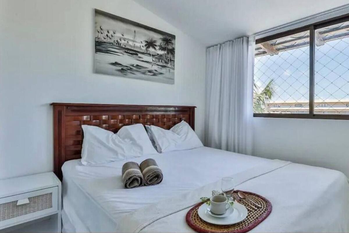 Ein ordentlich bezogenes Bett mit weißen Leinen, einem Holz-Kopfteil und einem Strandbild darüber.