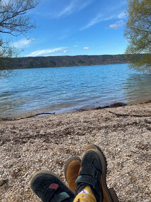 A view of a pebble beach with a lake and hills in the background.