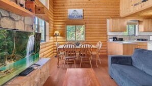 A log cabin interior with a dining table, chairs, a sofa, a television, and a kitchen area. - The Family Bear Cabin at Mt. Lemmon Hotel (Mount Lemmon)