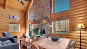 A log cabin interior with a dining table, chairs, a sofa, a fireplace, and a stone wall. - The Family Bear Cabin at Mt. Lemmon Hotel (Mount Lemmon)