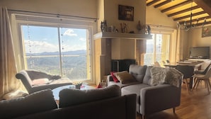 Un salon chaleureux avec une cheminée, un coin repas et une grande fenêtre offrant une vue panoramique.