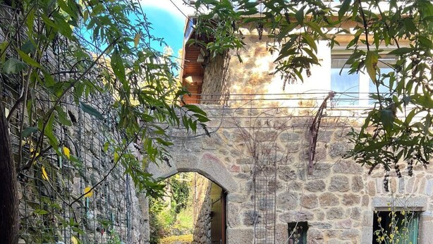 Une cour pavée de pierres, avec un mur en pierre rustique, une porte en bois et des plantes en pot.