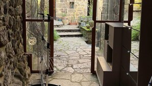 Une pièce aux murs de pierre, dotée d’une porte en verre qui donne sur un espace extérieur agrémenté d’un chemin de pierre et de verdure.