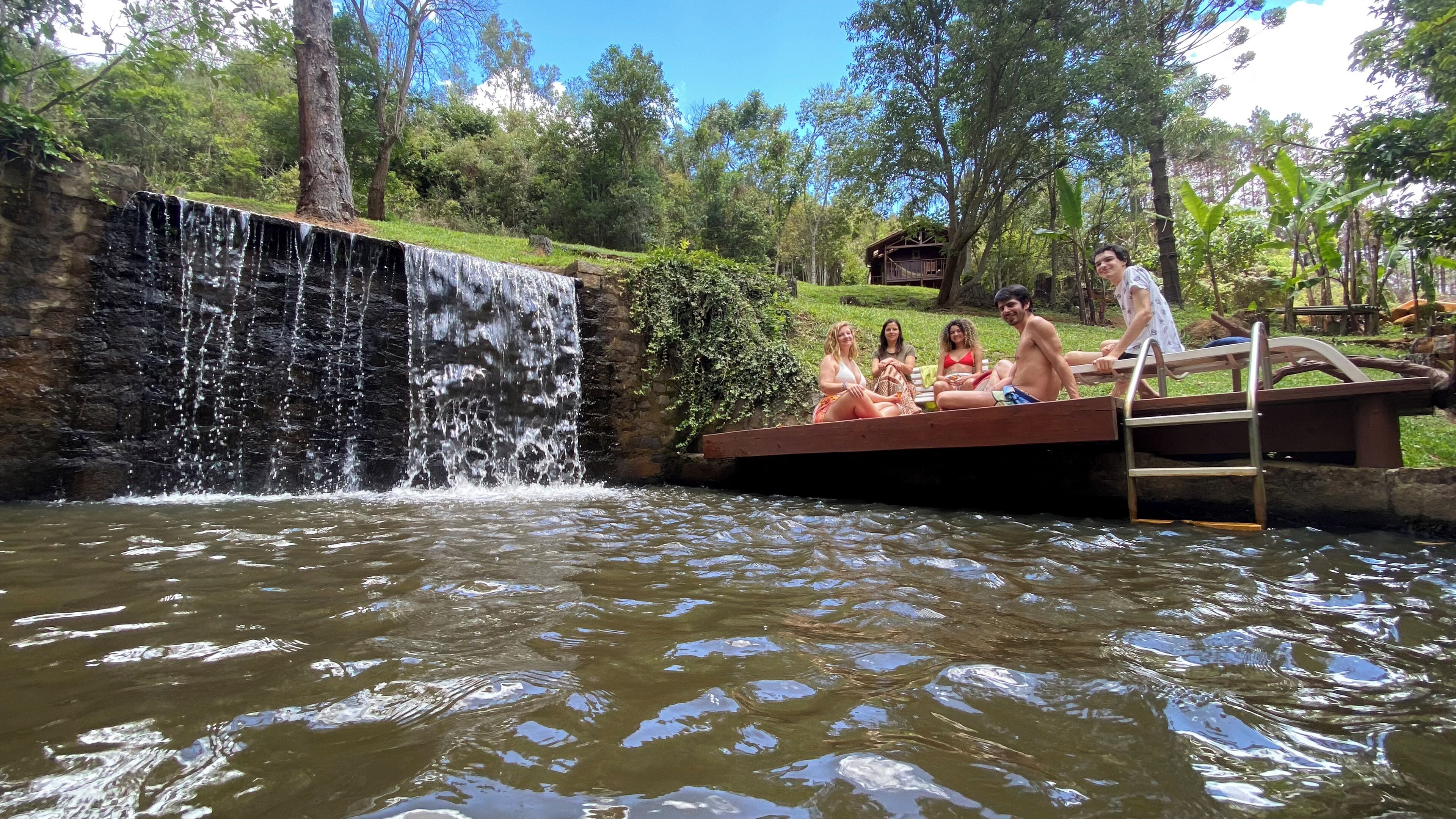 Um grupo de pessoas relaxando em um píer de madeira próximo a uma cachoeira.