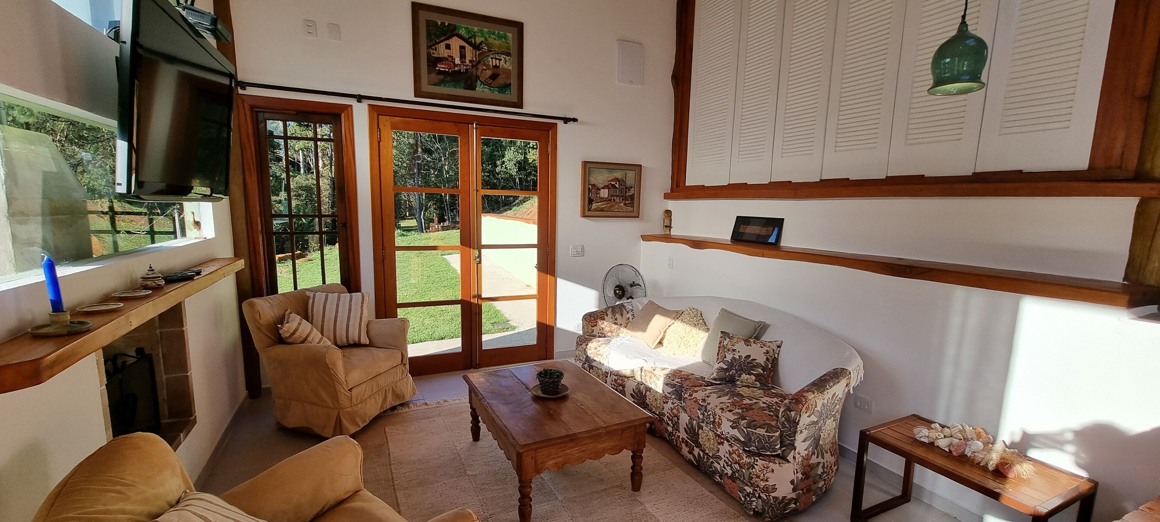 A cozy living room with a sofa, a coffee table, and a TV. There are wooden doors leading to a garden.